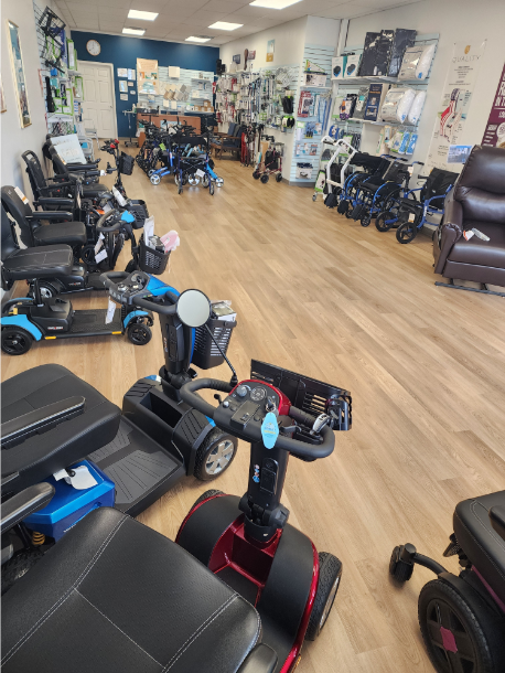 Image of inside of My Mobility retail store.  Photo is taken from the vantage point behind a power scooter to showcase the various products available at the retail site.